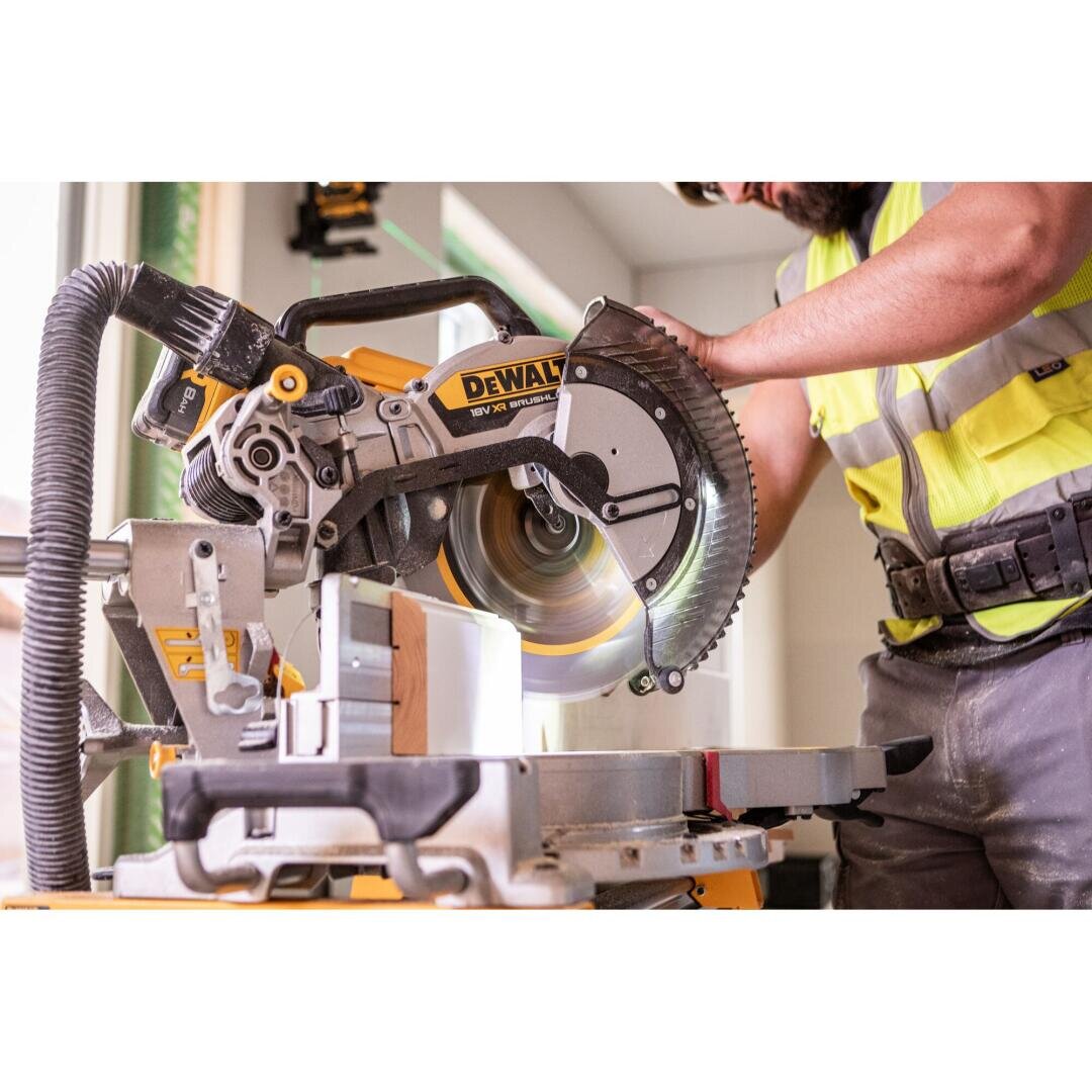 Eine Person in einer gelben Sicherheitsweste schneidet mit einer DeWalt-Gehrungssäge in einem Innenraum ein Holzstück zu, wobei sich das Sägeblatt dreht und der Arbeitsbereich gut beleuchtet ist.