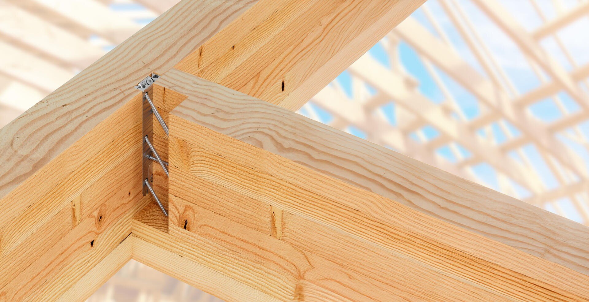 Nahaufnahme von Holzbalken, die im rechten Winkel mit einem verdeckten Verbinder miteinander verbunden sind, mit einem unscharfen Hintergrund, der eine Holzrahmenkonstruktion vor einem blauen Himmel zeigt.