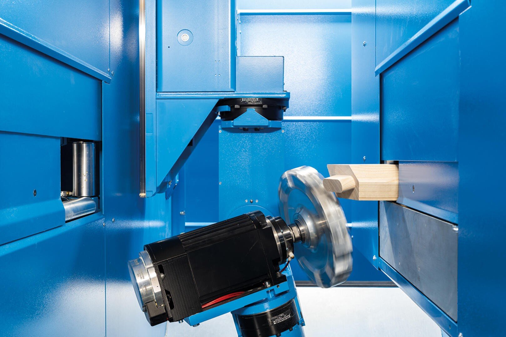 Eine CNC-Maschine mit einem sich drehenden Kreissägeblatt schneidet ein Stück Holz in einem blauen, geschlossenen Arbeitsbereich.
