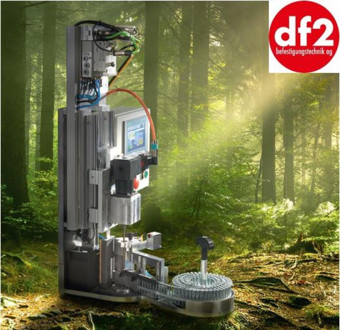 Eine komplexe Industriemaschine steht in einem sonnenbeschienenen Wald, die digitale Steuerung und Verkabelung ist sichtbar. In der rechten oberen Ecke befindet sich ein rot-weißes Logo mit df2 befestigungstechnik ag.