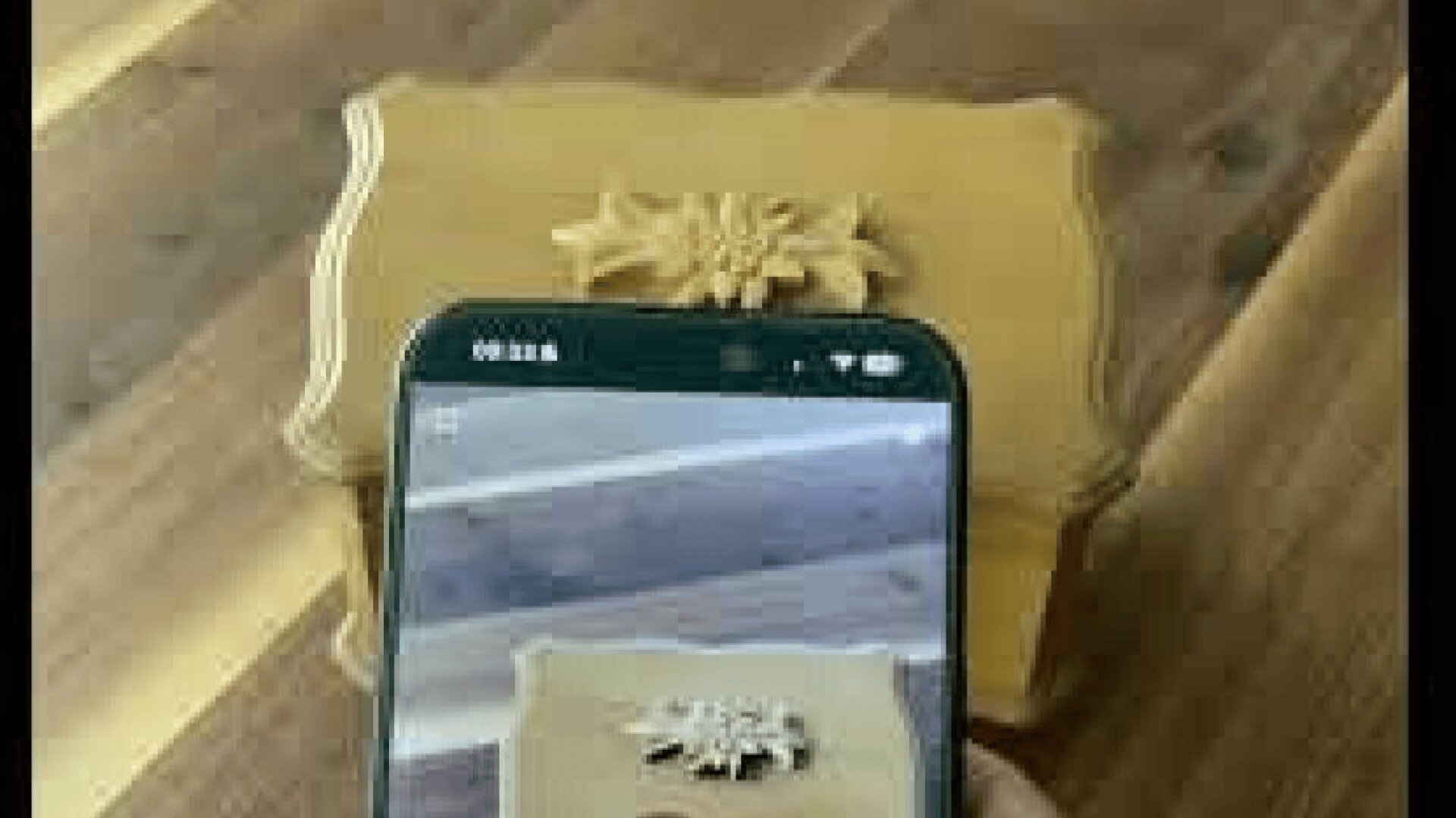 Ein Smartphone wird über eine dekorative Holzschachtel gehalten und nimmt ein Bild des verzierten Blumenmusters auf dem Deckel der Schachtel auf. Die Kiste steht auf einer Holzfläche.