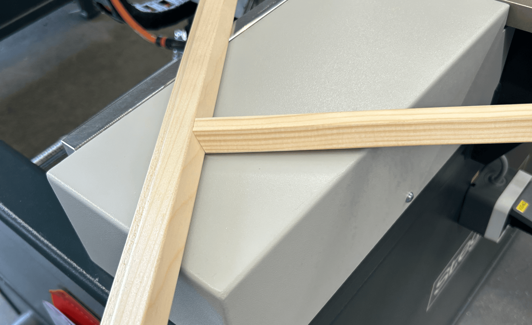 Dans un atelier, deux bandes de bois clair avec des bords à onglet précis sont placées au-dessus d'un équipement industriel de couleur grise.