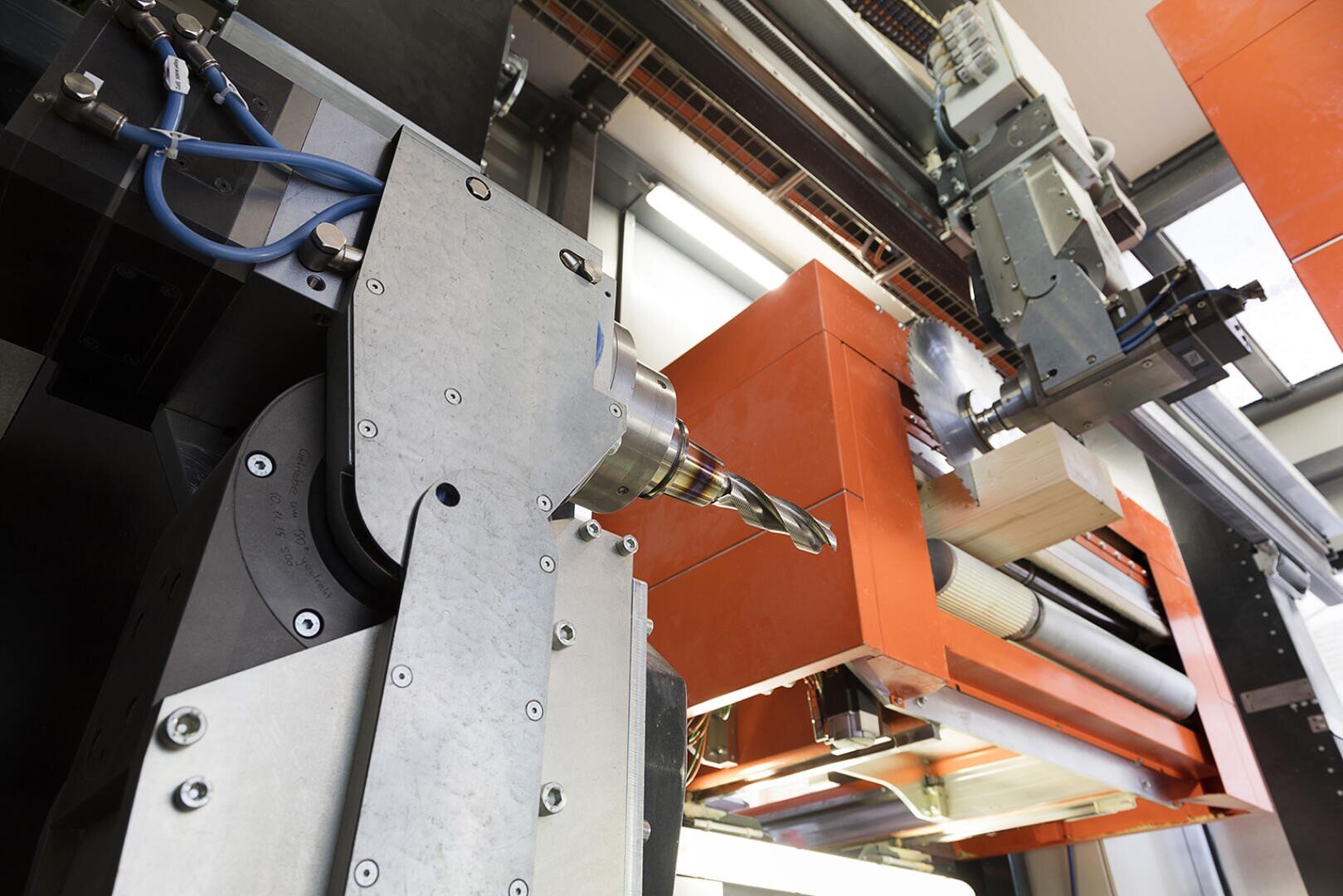 Gros plan sur une machine CNC industrielle équipée d'une perceuse, de composants métalliques et d'un carter orange, travaillant dans un environnement de production moderne sur un bloc de bois.