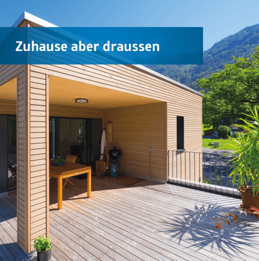 Eine moderne Holzterrasse mit Gartenmöbeln und Topfpflanzen, die an ein Haus angebaut ist, vor einer Kulisse aus grünen Bäumen und Bergen. Auf einem blauen Transparent steht "Zuhause aber draussen".