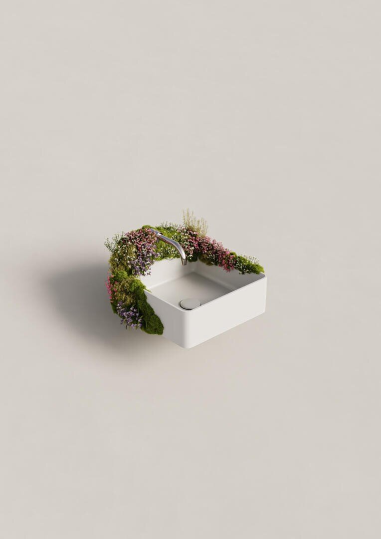 Ein modernes weißes Waschbecken steht auf einer glatten Fläche, über einer Ecke wächst ein Bogen aus grünem Moos und kleinen bunten Blumen, die einen natürlichen, dekorativen Rahmen bilden.