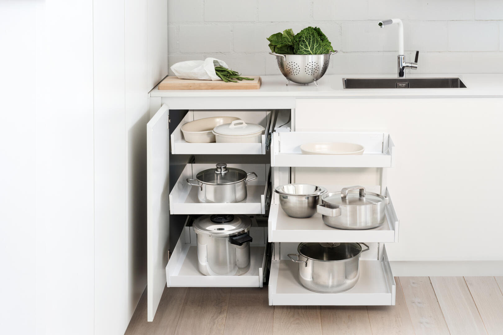 Une cuisine blanche avec un armoire d'angle ouvert et des étagères coulissantes.