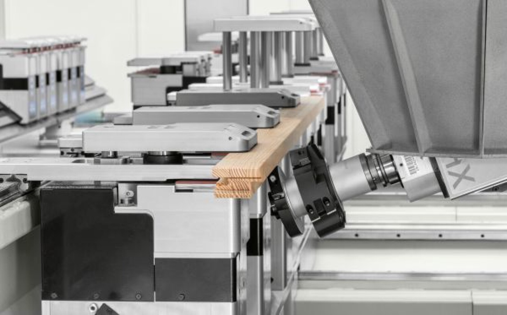 Ein Roboterarm positioniert ein Holzbrett mit ineinandergreifenden Verbindungen auf einem Metallmontageband in einer modernen Industrieumgebung.
