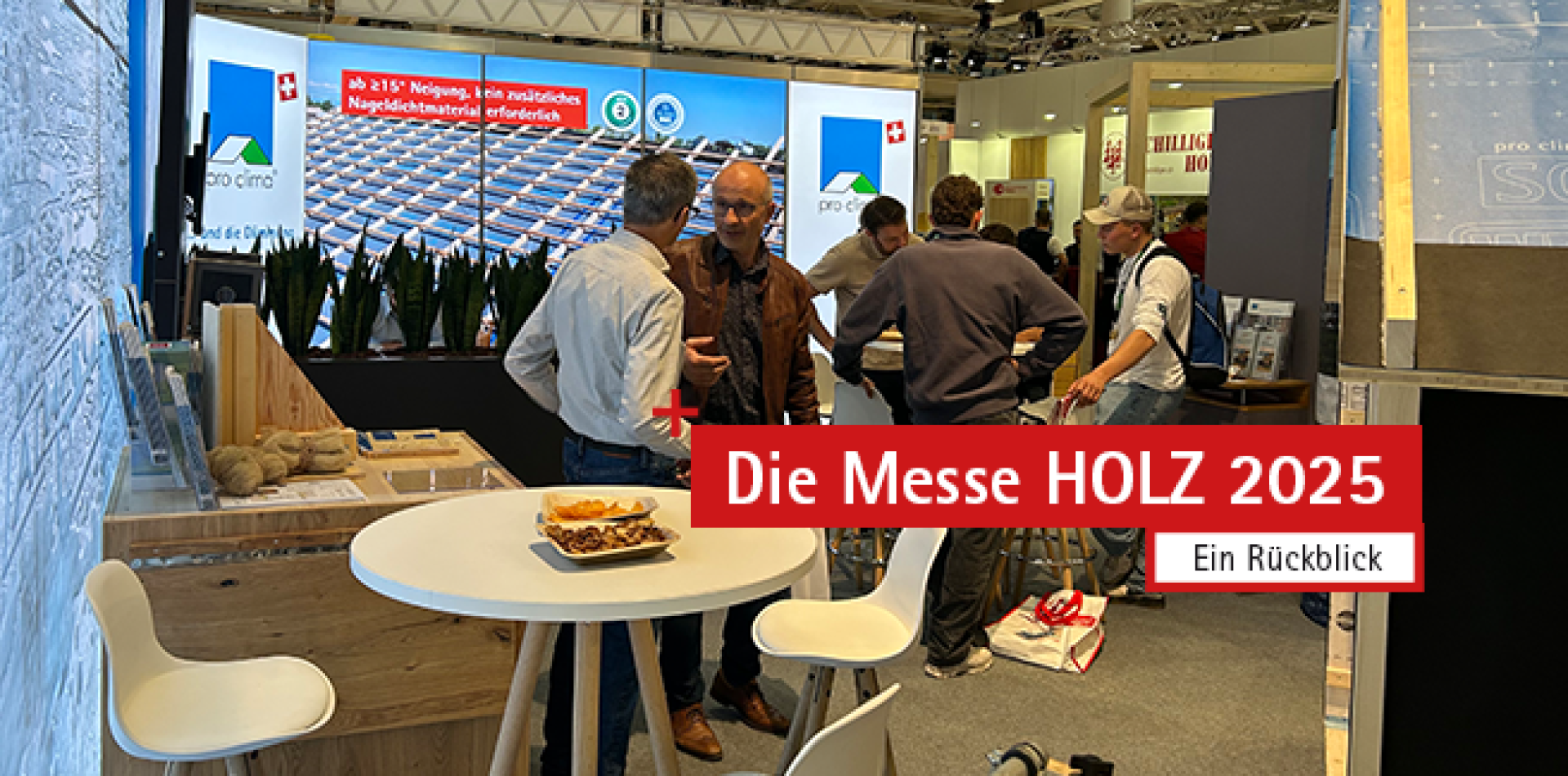 Menschen unterhalten sich an einem Messestand mit einer Ausstellung über Holzbau. Auf den Schildern steht "Die Messe HOLZ 2025" und "Ein Rückblick". Im Vordergrund steht ein Tisch mit Snacks und weißen Stühlen.