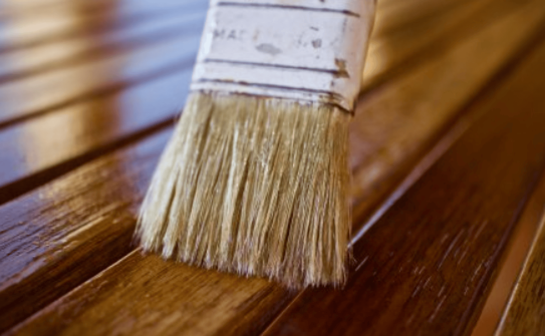 Gros plan d'un pinceau appliquant une lasure brillante sur des lattes de bois, mettant en évidence la surface humide et brillante à côté du bois sec.