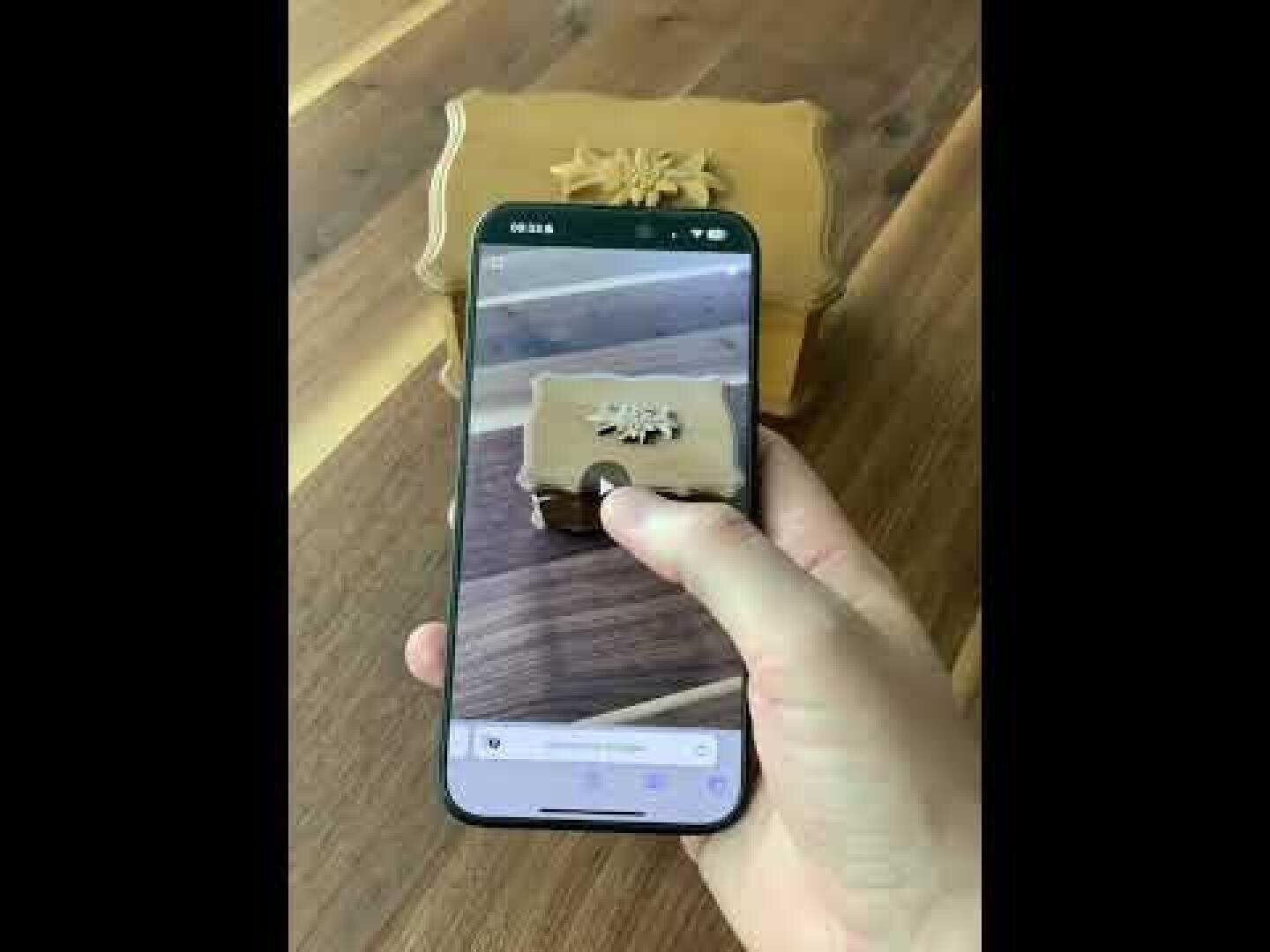 Une main tient un smartphone et prend une photo d'une boîte décorative en bois avec un motif sculpté sur le dessus, placée sur une surface en bois.