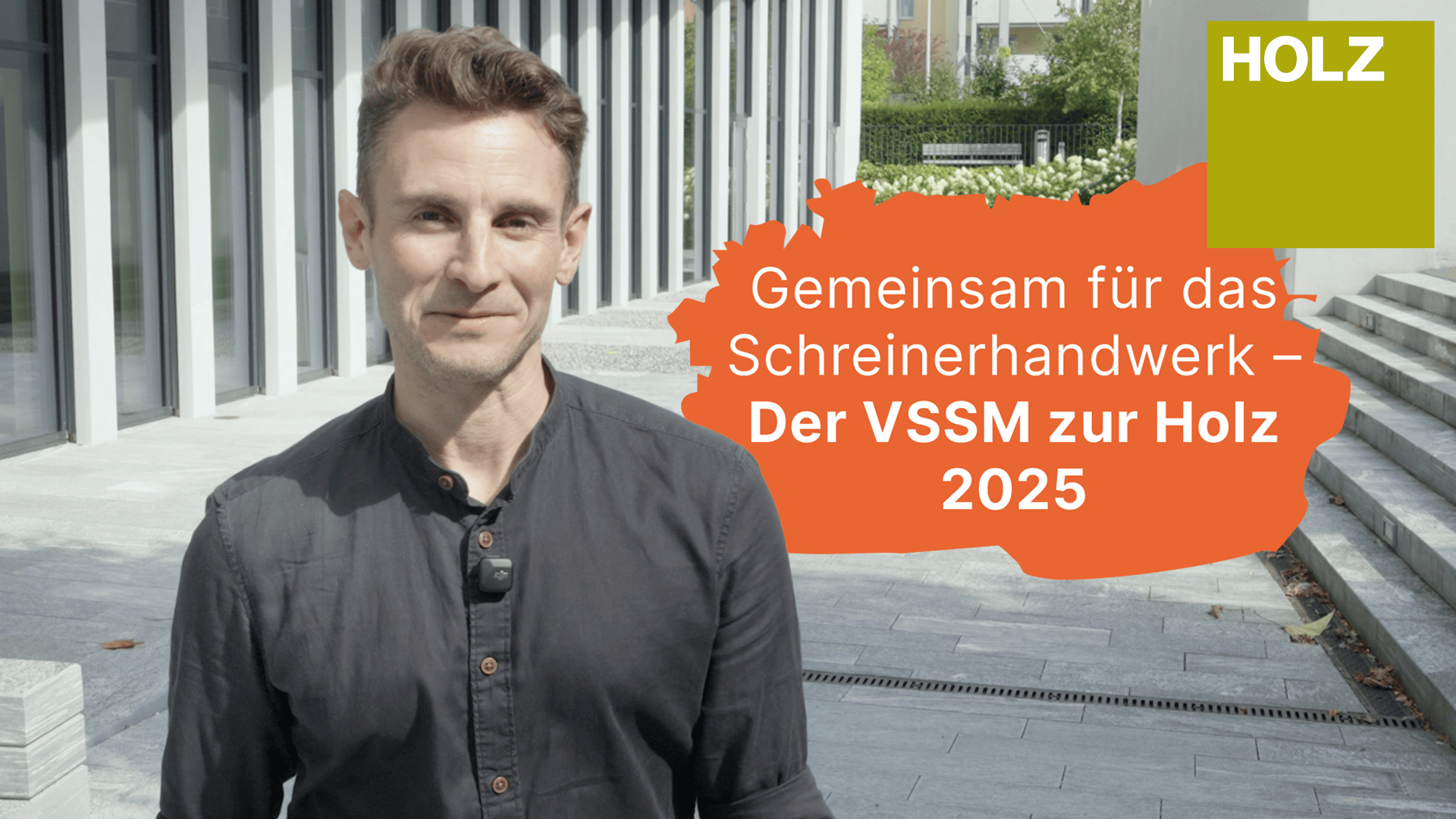 Ein Mann steht vor einem modernen Gebäude, trägt ein graues Hemd und ein Mikrofon. Neben ihm befindet sich ein orangefarbener Textkasten mit deutschem Text, der für VSSM und Holz 2025 wirbt, und ein grünes Quadrat in der oberen rechten Ecke mit der Aufschrift HOLZ.
