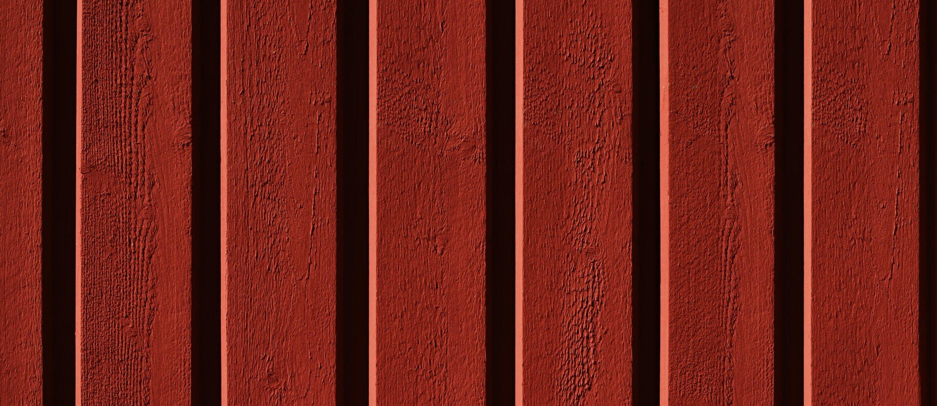 Senkrechte, gleichmäßig verteilte rote Holzbretter mit strukturierter Oberfläche und abwechselnd erhabenen und vertieften Abschnitten, die ein gestreiftes Muster ergeben.