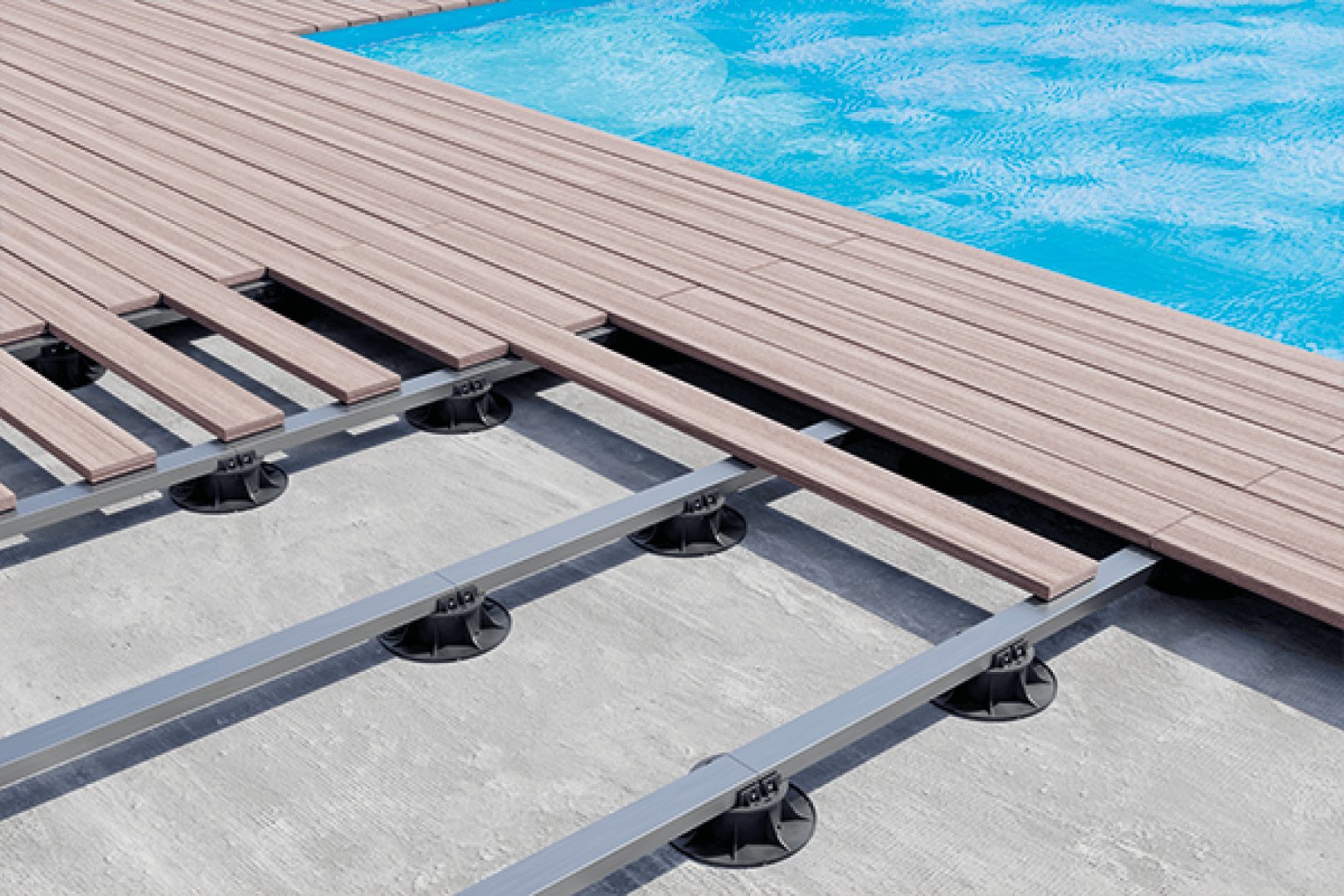 Nahaufnahme eines im Bau befindlichen Pooldecks, das Holzplanken zeigt, die teilweise über einem Metallrahmen mit schwarzen Stützsockeln über einer Betonfläche neben einem blauen Swimmingpool angebracht sind.