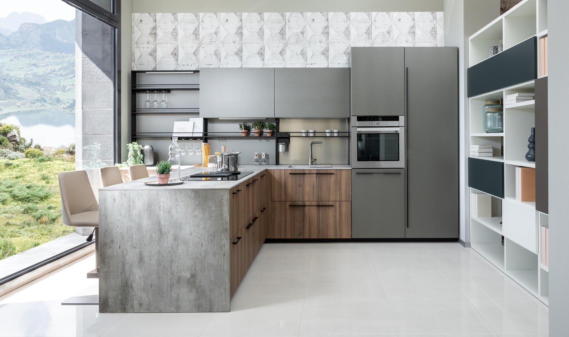 Moderne Küche mit grauen und Holzschränken, Einbaubackofen, Insel mit Barhockern, offenen Regalen und einem großen Fenster mit Blick auf die Berge und den See. Der Raum ist hell mit minimalistischem Dekor.