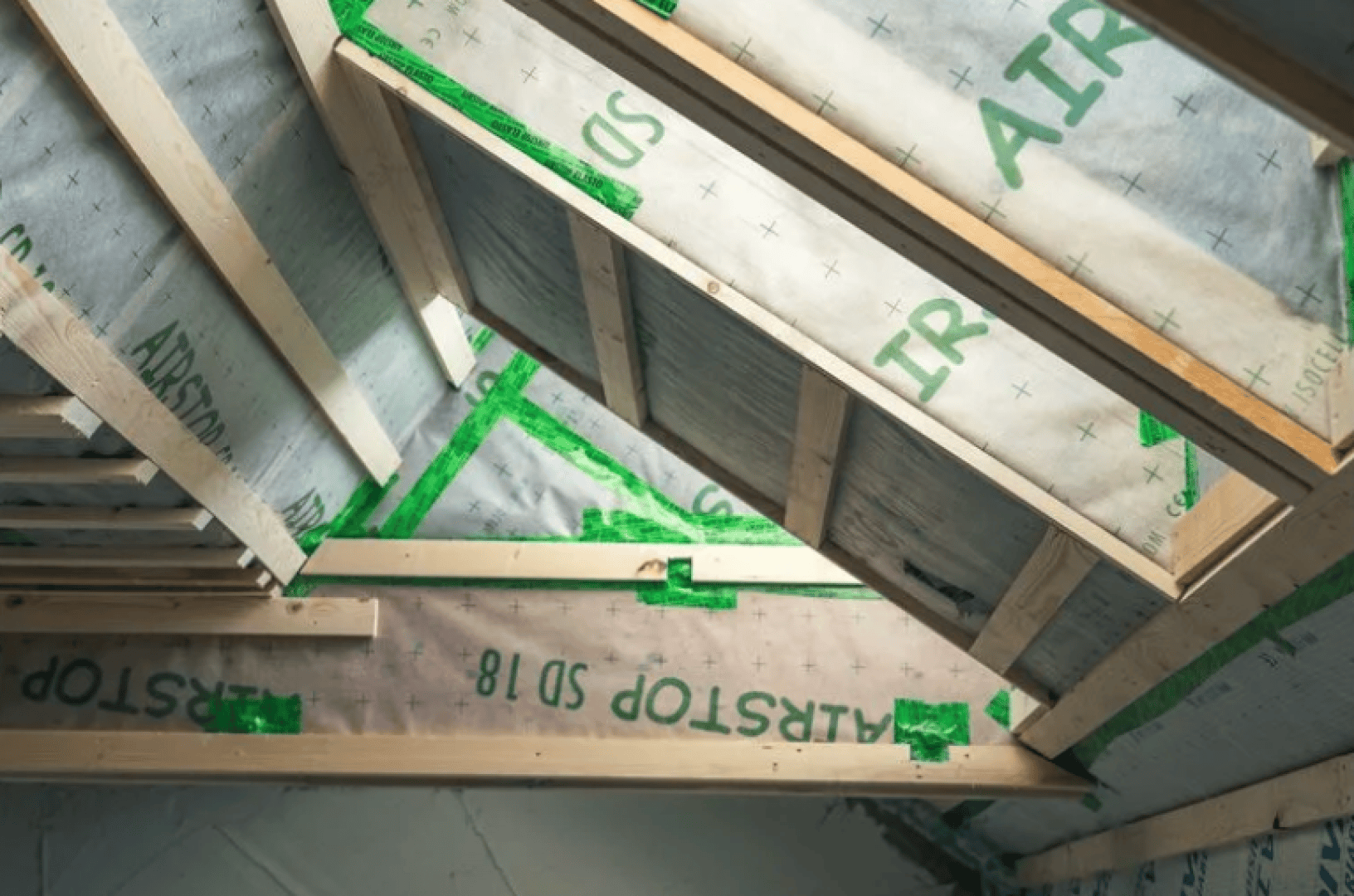 Schrägansicht einer im Bau befindlichen Decke mit Holzrahmen und Dämmplatten mit der Aufschrift AIRSTOP SD 18, befestigt mit grünem Klebeband.