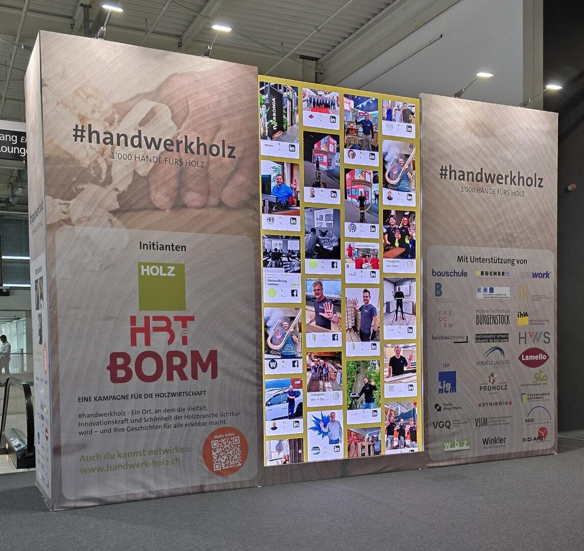 Sur un grand présentoir d'exposition, on peut voir le hashtag #handwerkholz, les logos de la campagne, les sponsors partenaires et un collage de contributions des médias sociaux sur le thème du travail du bois, avec des codes QR et des panneaux d'information de chaque côté.