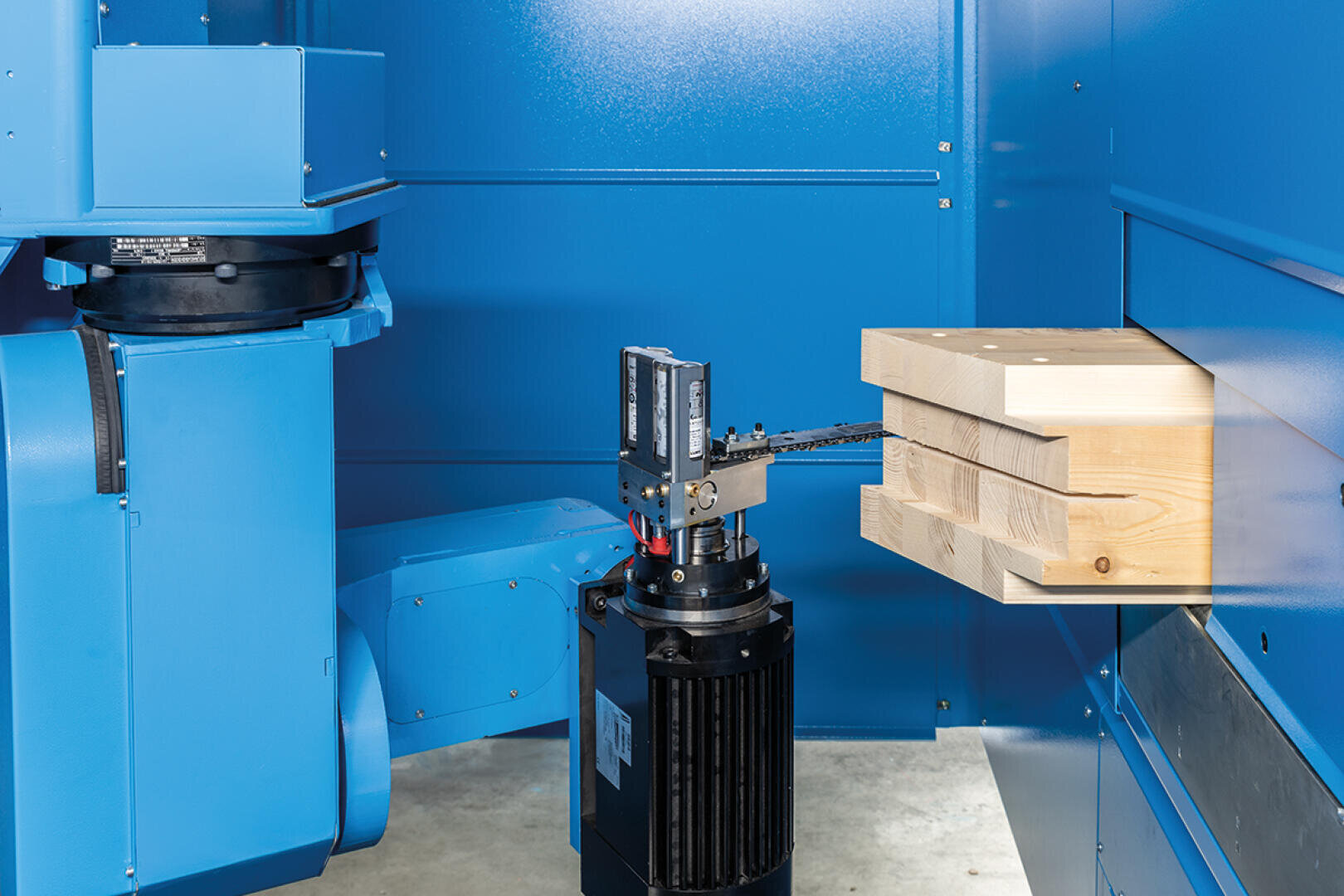 Ein blauer Industrieroboterarm positioniert ein Werkzeug neben zwei gestapelten Holzbrettern in einer Produktionsstätte mit blauen Metallwänden.