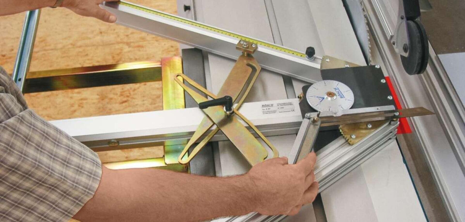 Eine Person justiert ein Winkelmessgerät an einer Tischkreissäge mit Metallrahmen, um das Material für einen präzisen Schnitt auszurichten. Messmarkierungen und ein winkelmesserähnliches Gerät sind sichtbar.