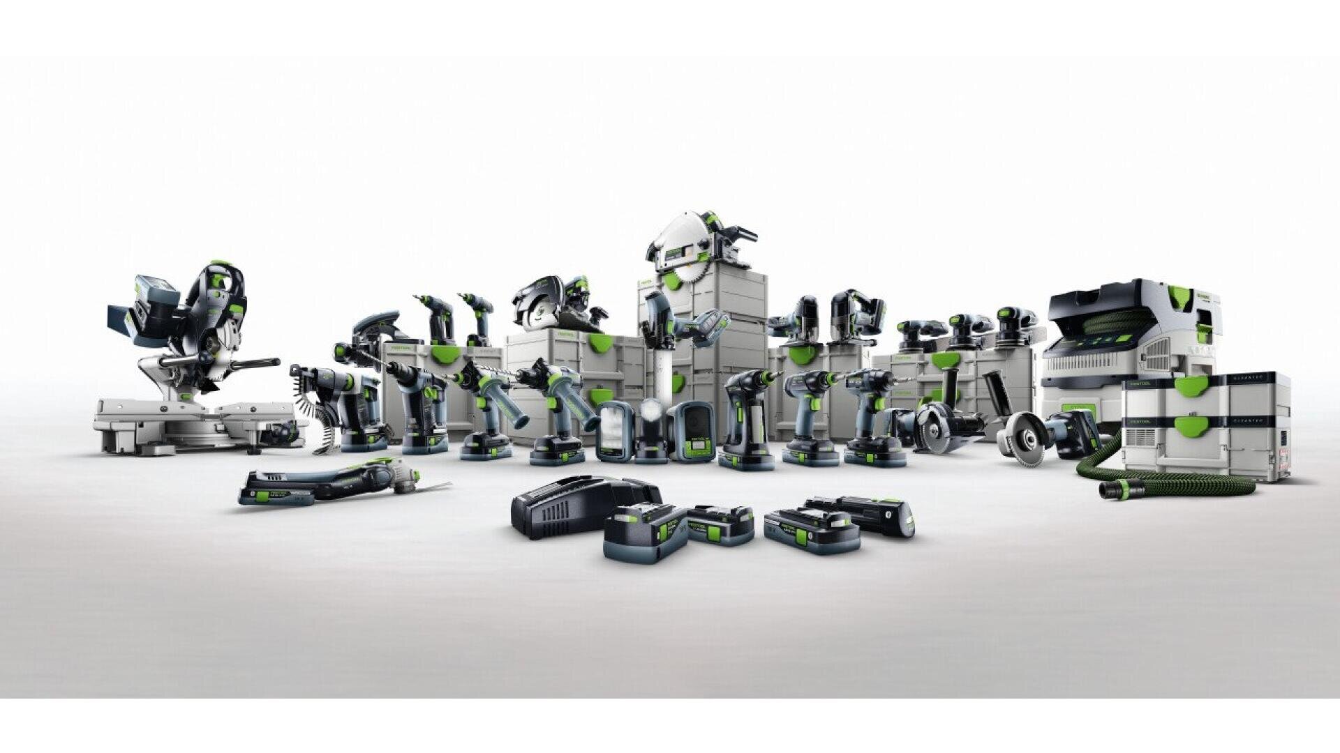 Une collection d'outils électriques et d'accessoires Festool disposés en rang sur un fond blanc, comprenant des scies, des perceuses, des ponceuses, des batteries et des boîtes de rangement avec des accents verts.