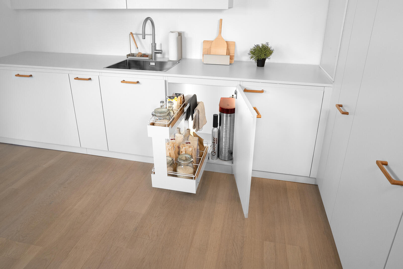 Une cuisine blanche moderne avec des poignées en bois et une armoire coulissante avec des verres, des bouteilles et des serviettes à côté d'un appareil de traitement de l’eau.
