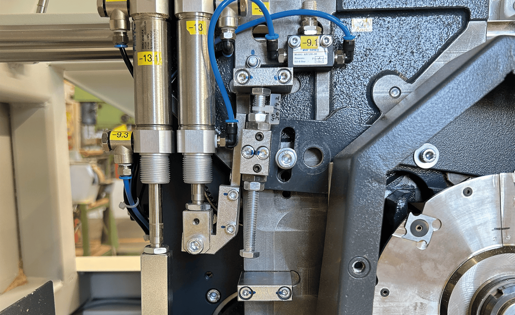 Gros plan sur une machine industrielle avec des composants métalliques, des cylindres, des boulons, des fils bleus et des pièces étiquetées, qui font probablement partie d'un système mécanique ou de fabrication plus important.