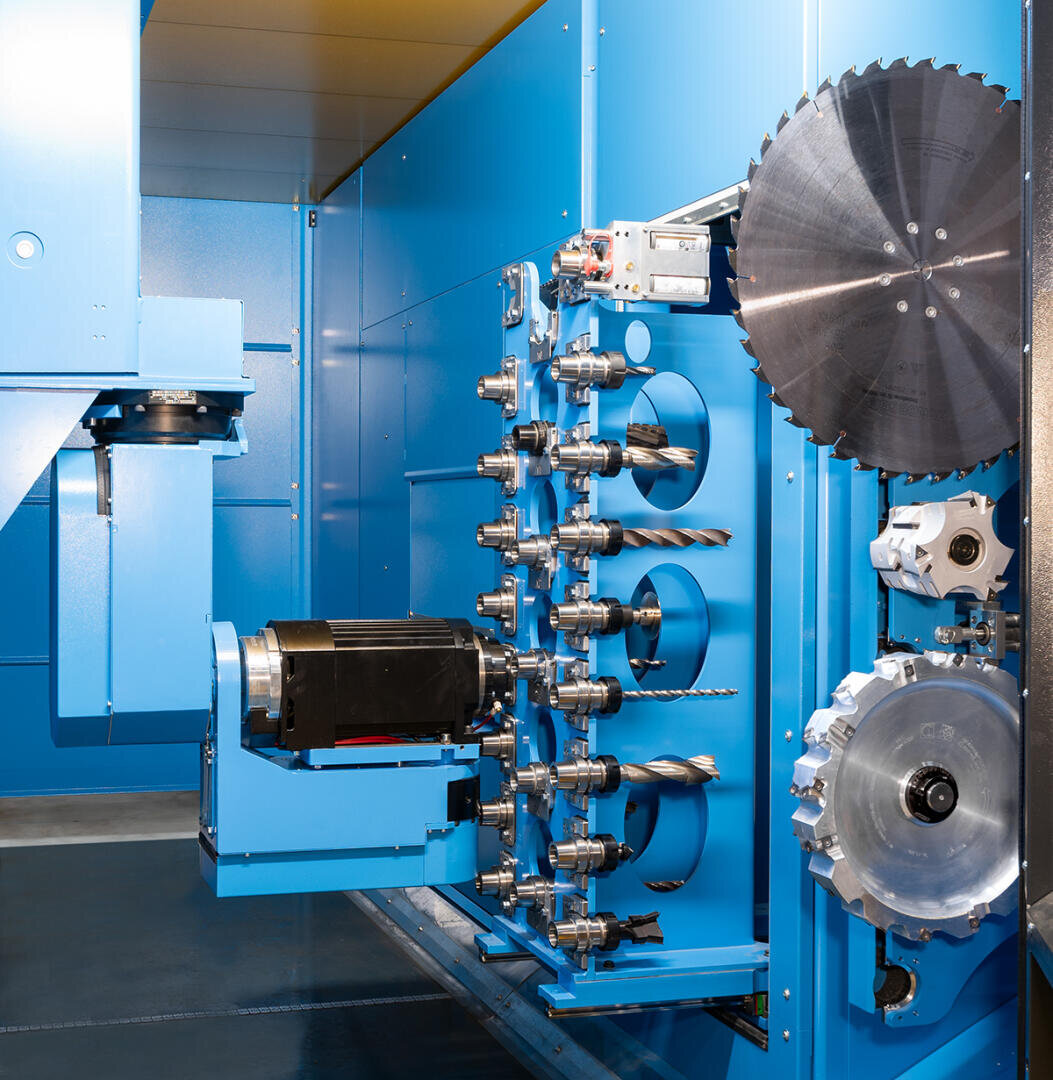 Nahaufnahme einer blauen industriellen CNC-Maschine mit mehreren Bohrern, einem Kreissägeblatt und verschiedenen Schneidwerkzeugen, die auf einem rotierenden Revolver in einem sauberen, hell beleuchteten Arbeitsbereich angeordnet sind.