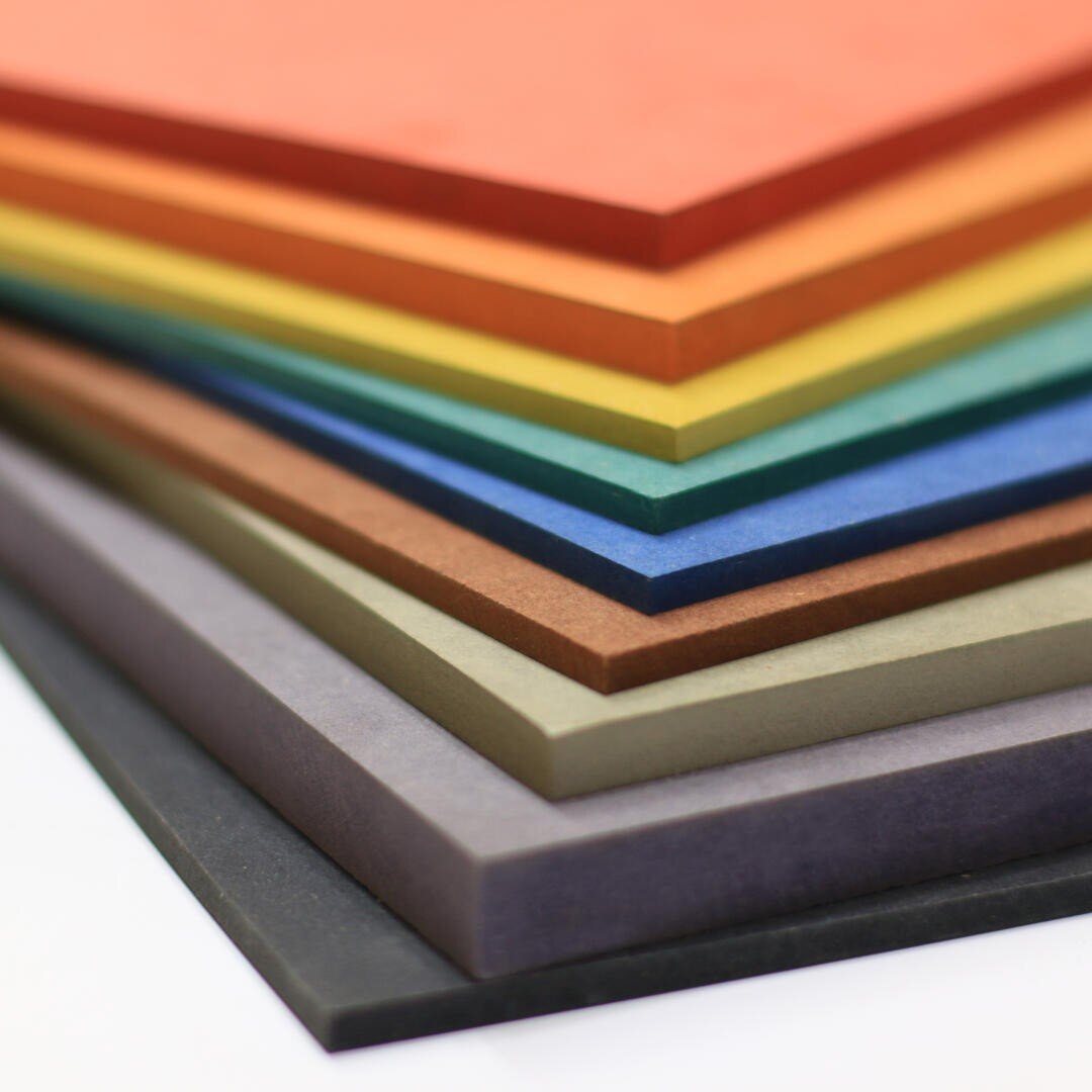 Une pile de feuilles rectangulaires de différentes couleurs, notamment rouge, orange, jaune, vert, bleu, gris, brun et noir, disposées proprement les unes sur les autres sur un fond blanc.