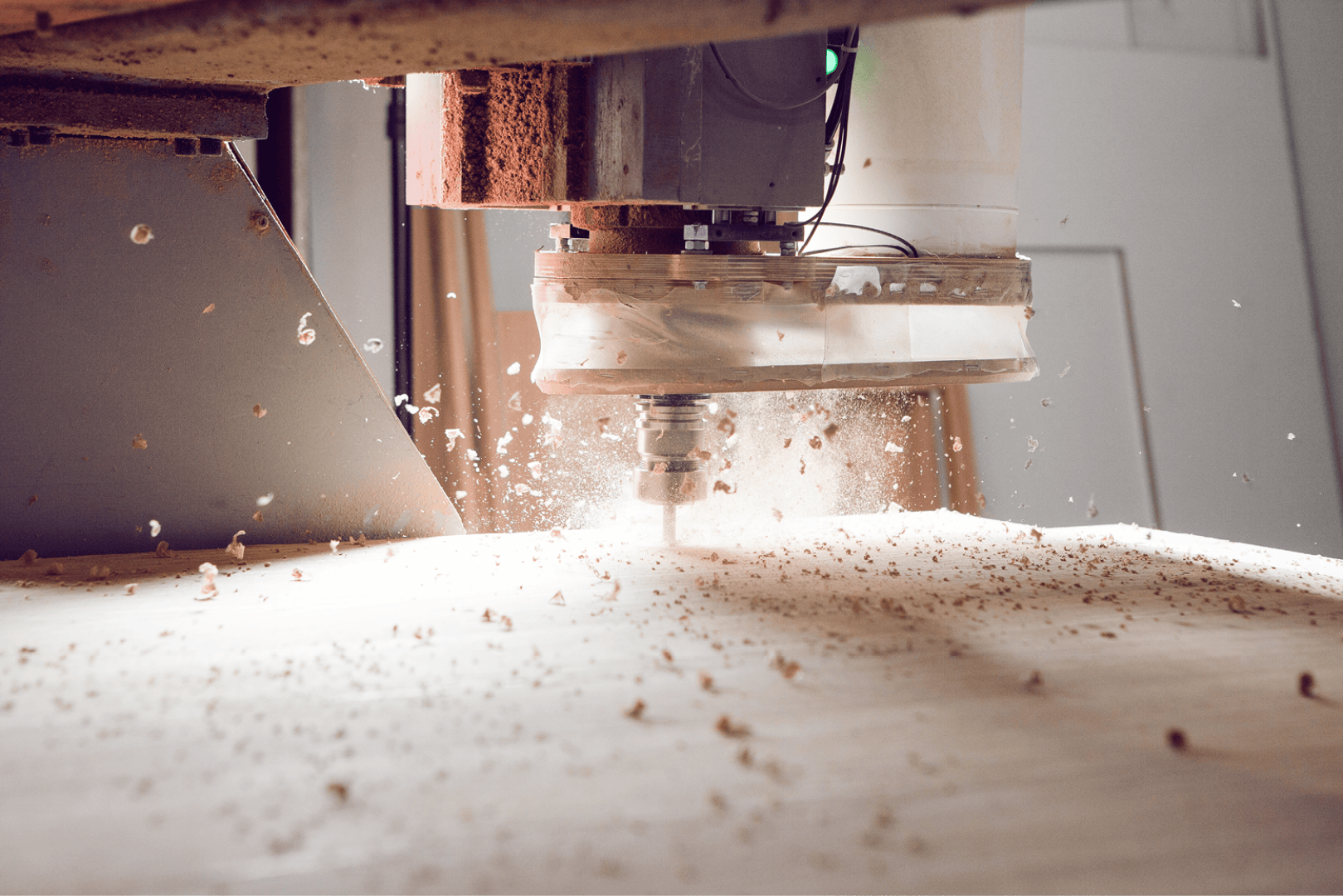 Gros plan d'une machine CNC en train de découper une surface en bois, avec des copeaux et de la poussière projetés autour de l'outil de coupe rotatif. L'image capture le mouvement et la précision du travail du bois.