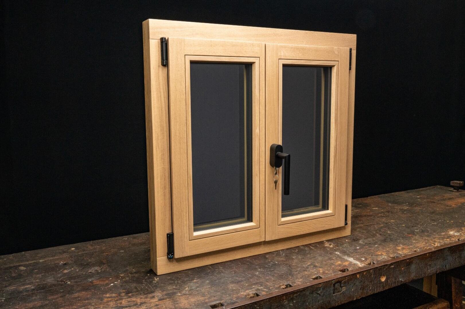 Ein holzgerahmtes Doppelglasfenster mit schwarzem Griff und Schlüssel, das aufrecht auf einem abgenutzten Holztisch vor einem schlichten schwarzen Hintergrund steht.