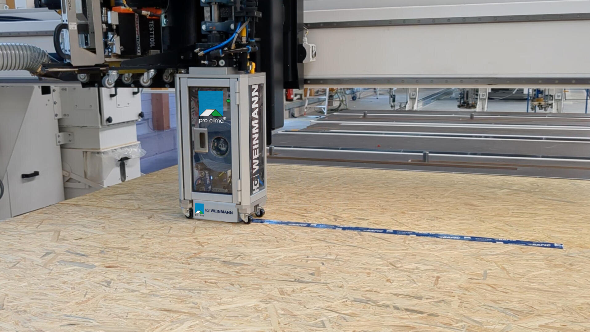 Eine Nahaufnahme einer industriellen CNC-Maschine mit der Bezeichnung WEINMANN, die in einer Fabrik an einer großen Platte aus Grobspanplatten (OSB) arbeitet, im Hintergrund sind Werkzeuge und Maschinen zu sehen.