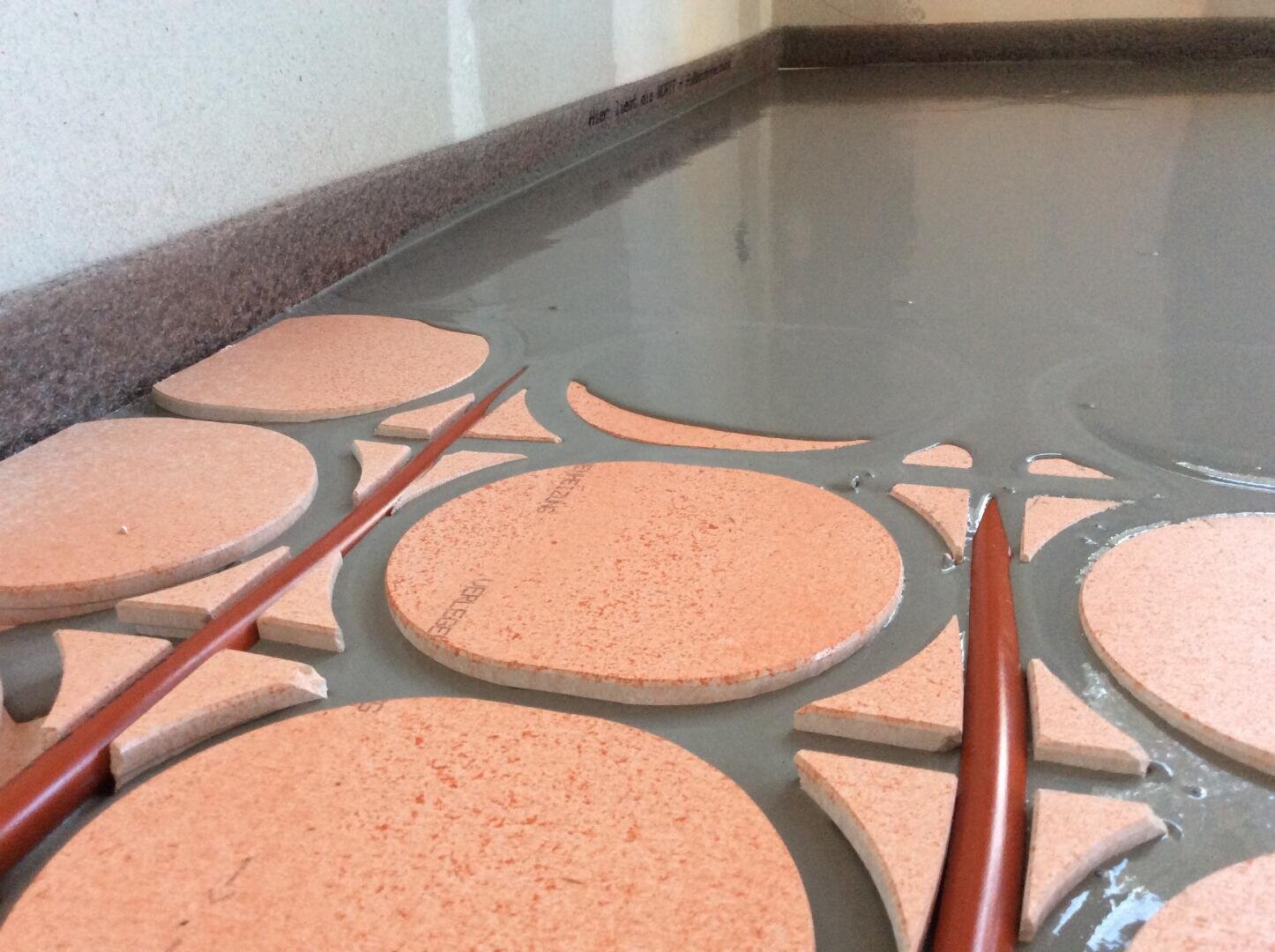 Nahaufnahme von orangefarbenen Fußbodenheizungsrohren und runden Dämmplatten, die in einem im Bau befindlichen Raum mit feuchtem Beton bedeckt werden.