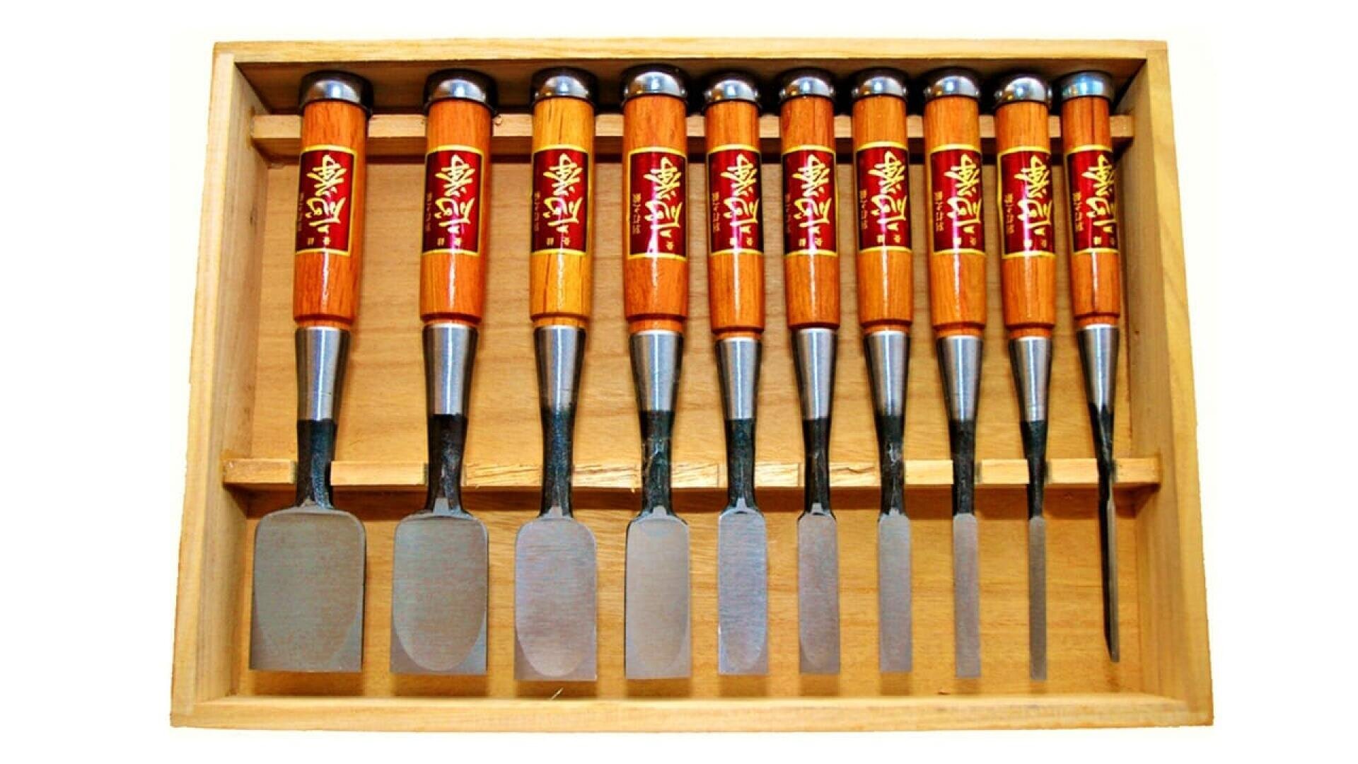 Coffret en bois contenant un ensemble de neuf ciseaux à poignées en bois poli et à lames en métal, disposés en rangée de la plus large à la plus étroite. Chaque manche porte une étiquette décorative rouge et or.