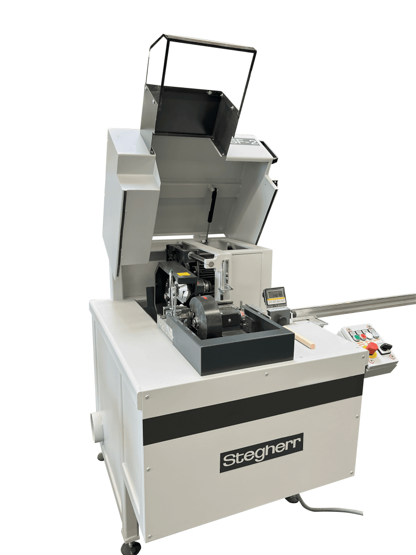 Une grande machine industrielle avec un couvercle supérieur partiellement ouvert, un panneau de commande et un écran. La machine porte le nom de la marque Stegherr sur sa face avant et est utilisée pour des processus de fabrication ou de découpe automatisés.