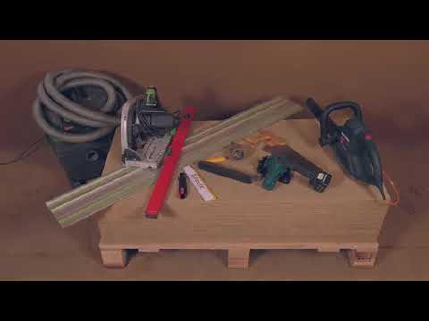 Une palette en bois contient divers outils, dont une scie circulaire, un rabot électrique, un niveau rouge, une règle pliante, un mètre ruban, un crayon, des pinces et un tuyau d'aspirateur enroulé, le tout sur un fond marron.