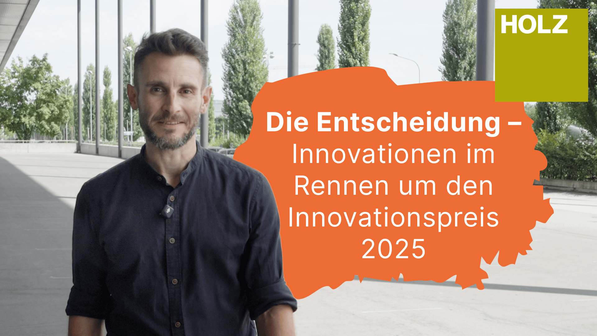 Un homme se tient à l'extérieur, près d'un bâtiment moderne. À côté de lui, un graphique orange avec un texte en allemand sur les innovations en lice pour le prix de l'innovation 2025 et un carré vert avec HOLZ en lettres blanches.