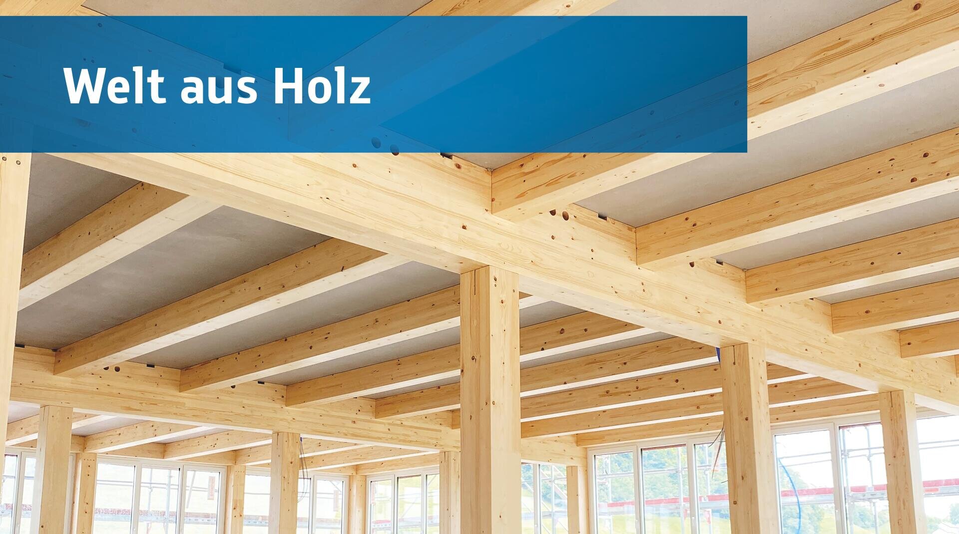 Holzbalken und -säulen bilden die Struktur eines modernen Gebäudeinneren mit großen Fenstern; ein blaues Banner oben links trägt die Aufschrift Welt aus Holz in weißer Schrift.