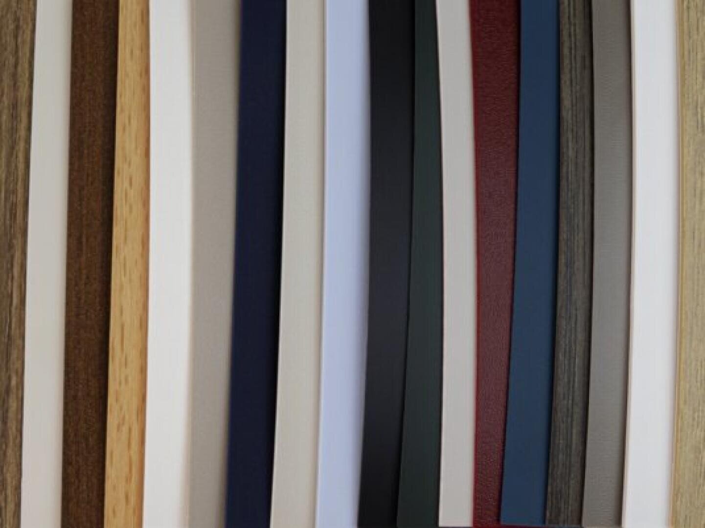 Une sélection de bandes verticales de différentes textures et couleurs, notamment des tons de beige, de brun, de gris, de blanc, de noir, de rouge et de bleu, qui peuvent représenter des motifs de matériaux stratifiés ou de placage.