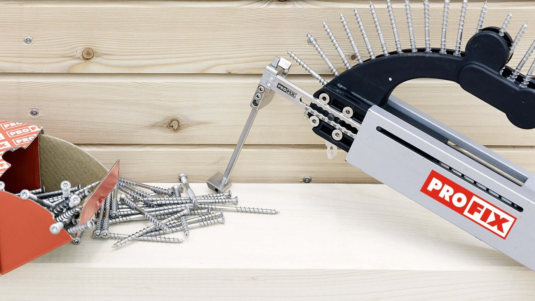 Ein automatischer PROFIX-Schraubendreher mit einem Streifen Schrauben steht neben einer Kiste, aus der lose Schrauben auf eine Holzfläche mit einem hellen Holzbrett als Hintergrund fallen.