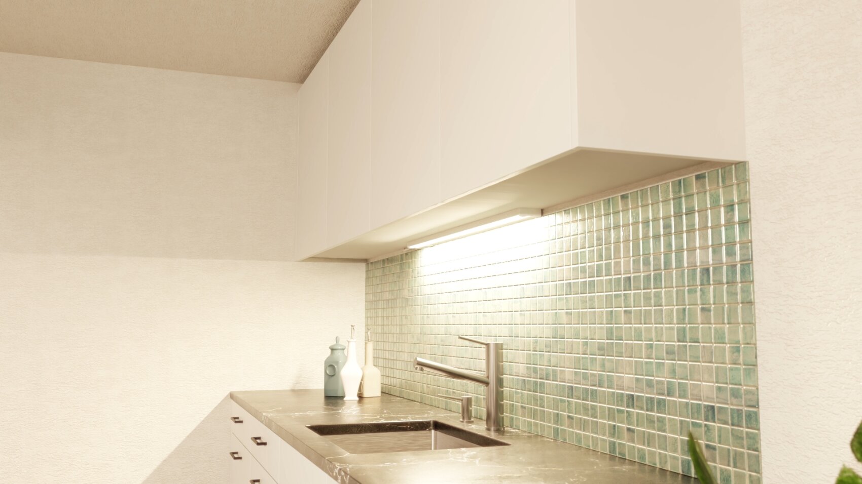 Moderne Küche mit weißen Schränken, einer dunklen Arbeitsplatte, einer Spüle aus Edelstahl und einer grün gefliesten Aufkantung. Dekorative Vasen stehen in der Nähe der Wand unter einer hellen Unterschrankbeleuchtung.